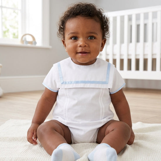 Carriage Boutique baby boy wearing a white bubble romper with blue trim, Peter Pan collar, and matching blue socks.