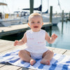 Carriage Boutique white picque baby boy bubble romper with sailboat embroidery, sitting on a striped towel.