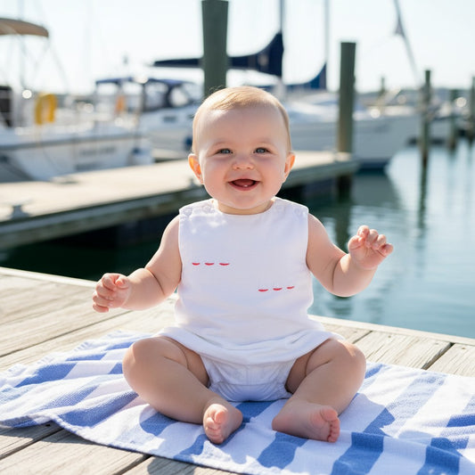 Carriage Boutique white picque baby boy bubble romper with sailboat embroidery, sitting on a striped towel.
