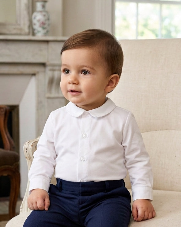 Carriage Boutique baby boy wearing a white long sleeve button-down shirt with a rounded collar sitting on a chair