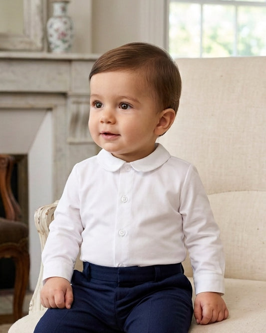 Carriage Boutique baby boy wearing a white long sleeve button-down shirt with a rounded collar sitting on a chair