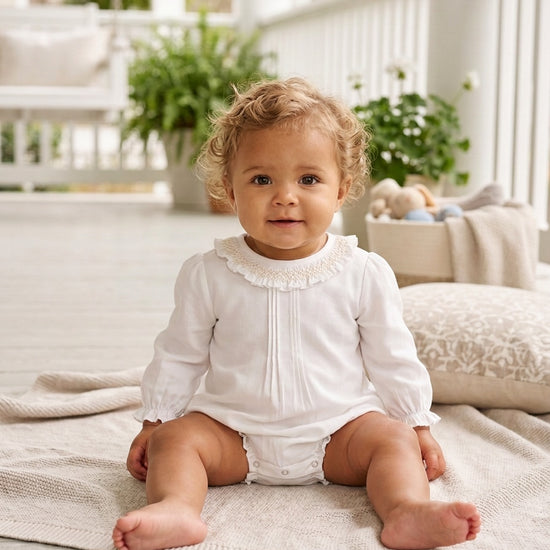 Carriage Boutique baby girl white long sleeve bubble romper with smocked collar sitting on a porch blanket