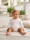 Carriage Boutique baby girl white long sleeve bubble romper with smocked collar sitting on a porch blanket