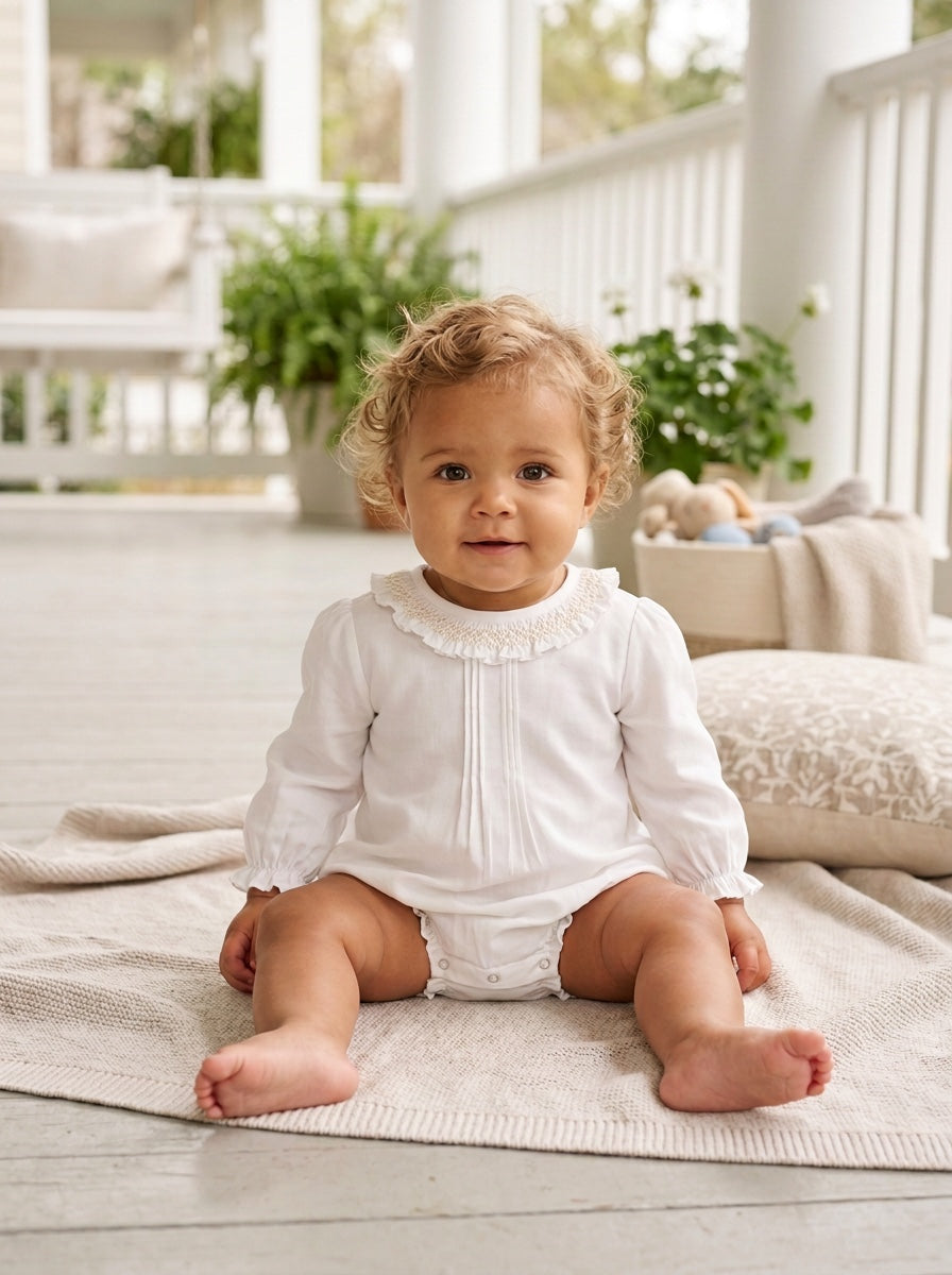 Carriage Boutique baby girl white long sleeve bubble romper with smocked collar sitting on a porch blanket
