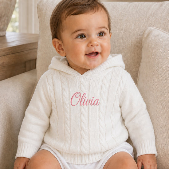Carriage Boutique white cotton cable knit hooded baby sweater with personalized pink embroidery on the chest.