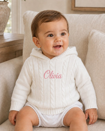 Carriage Boutique white cotton cable knit hooded baby sweater with personalized pink embroidery on the chest.