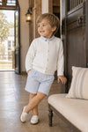 Carriage Boutique white cable-knit cotton cardigan worn by a young boy with a light blue shirt and shorts