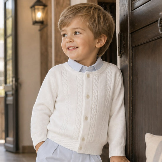 Carriage Boutique white cable-knit cotton cardigan on a young boy wearing a light blue shirt and trousers