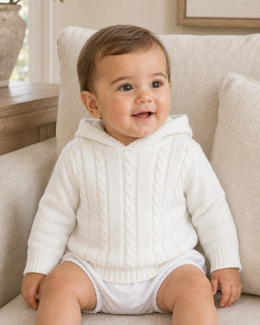 Carriage Boutique white cable knit hooded baby sweater made of soft cotton worn by a smiling baby