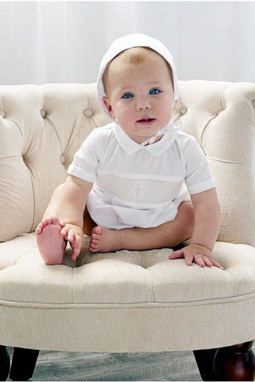 Carriage Boutique baby boy white christening bubble romper with smocked cross detail and matching bonnet on chair