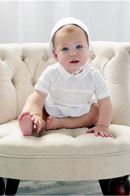 Carriage Boutique baby boy white christening bubble romper with smocked cross detail and matching bonnet on chair