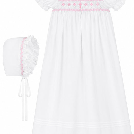 Carriage Boutique white christening gown with pink hand-smocked yoke, embroidered cross, and matching ruffled bonnet.