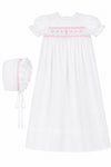 Carriage Boutique white christening gown with pink hand-smocked yoke, embroidered cross, and matching ruffled bonnet.