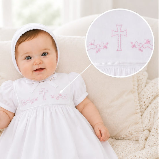 Carriage Boutique white baby christening gown with pink cross embroidery and matching bonnet on an infant