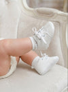 Carriage Boutique white baby boy christening shoes with cross embroidery and lace-up closure on a soft chair