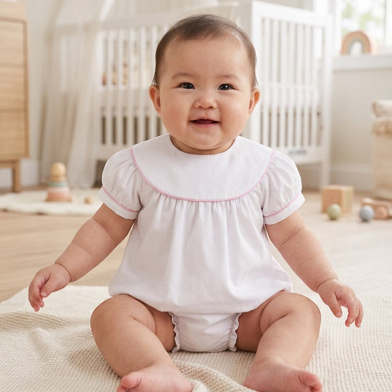Carriage Boutique white cotton baby girl bubble romper with flutter sleeves and pink picot trim in a nursery setting