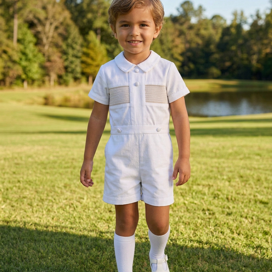 Carriage Boutique white cotton bobby suit with hand smocked detail, Peter Pan collar, and satin buttons on a young boy