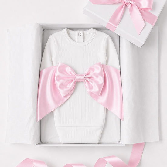 Carriage Boutique white cotton newborn swaddle bag featuring a large pink satin bow in a gift box with ribbon.