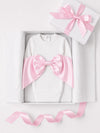 Carriage Boutique white cotton newborn swaddle bag featuring a large pink satin bow in a gift box with ribbon.