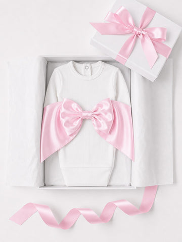 Carriage Boutique white cotton newborn swaddle bag featuring a large pink satin bow in a gift box with ribbon.