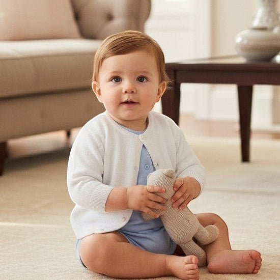 Carriage Boutique baby girl wearing a white cotton cashmere cardigan with ribbed hems over a light blue onesie