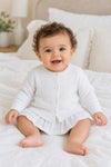 Carriage Boutique baby girl wearing a white cotton cashmere cardigan with ribbed hems and button front on a bed