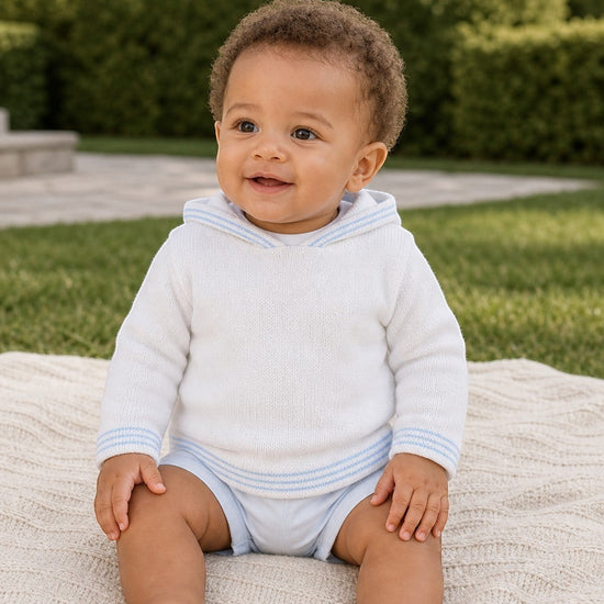 Carriage Boutique baby boy wearing a white hooded cotton sweater with light blue striped trim, sitting on a blanket.