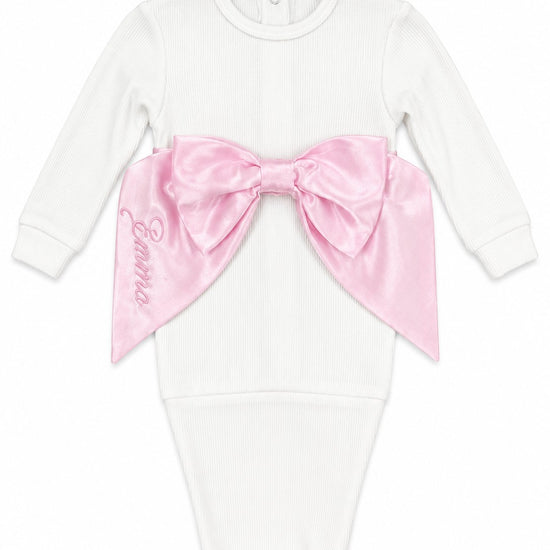Carriage Boutique white cotton newborn swaddle bag featuring a large pink satin bow and personalized embroidery.
