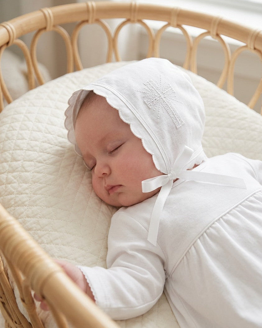 Carriage Boutique white cotton christening bonnet with embroidered cross, scalloped edge, and satin ribbon tie on baby