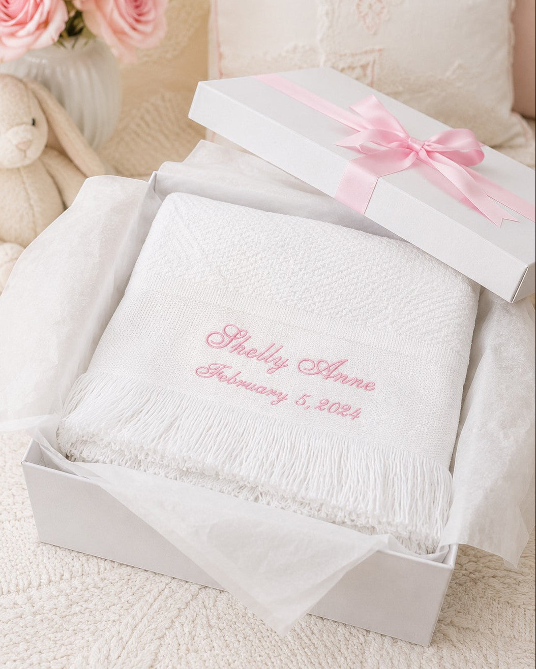 Carriage Boutique white knit baby blanket with pink personalized embroidery and fringe in a gift box with pink ribbon.