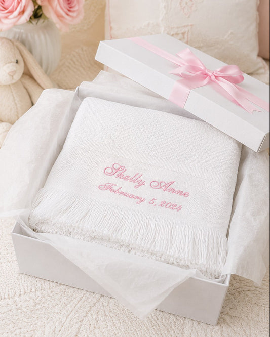 Carriage Boutique white knit baby blanket with pink personalized embroidery and fringe in a gift box with pink ribbon.