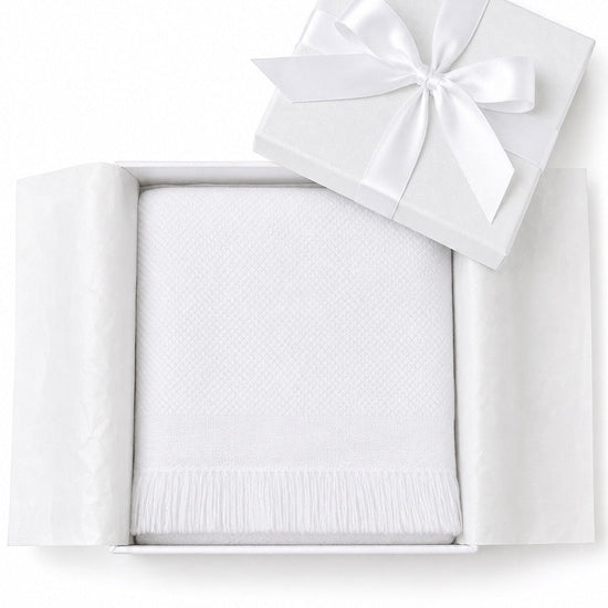 Carriage Boutique white knit baby blanket with fringe detail, presented in a gift box with a satin ribbon.