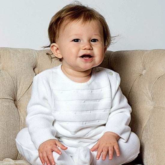 Carriage Boutique white knit 3-piece baby bris outfit with matching bonnet worn by a smiling baby in a chair