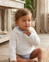 Carriage Boutique white knit baby boy hoodie with hood, worn by a toddler in a bright, rustic indoor setting.