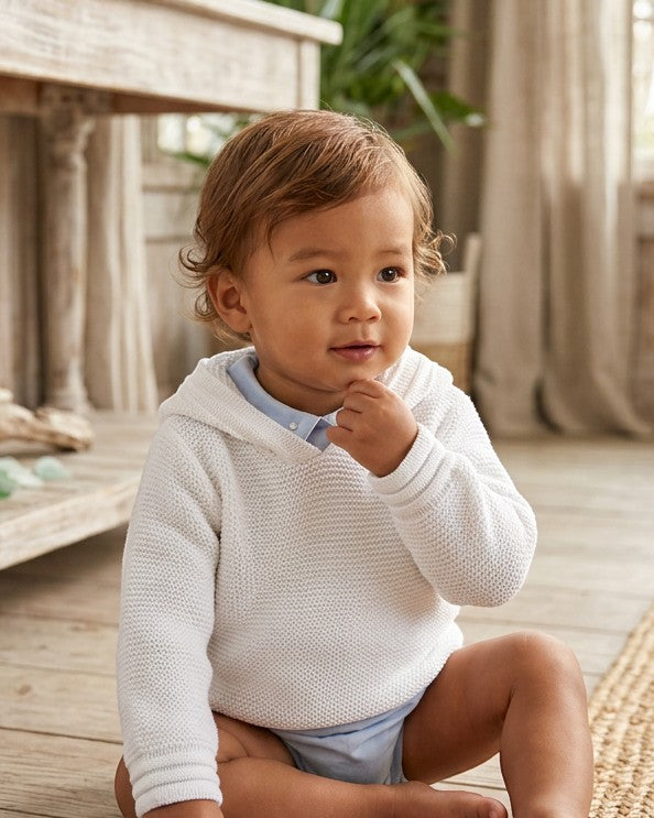 Carriage Boutique white knit baby boy hoodie with hood, worn by a toddler in a bright, rustic indoor setting.