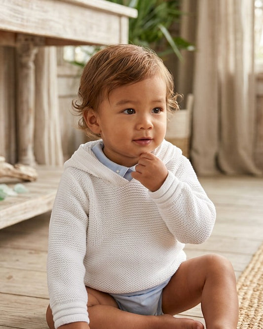 Carriage Boutique white knit baby boy hoodie with hood, worn by a toddler in a bright, rustic indoor setting.