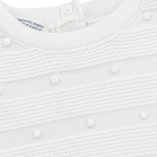 Carriage Boutique white knit baby bris outfit featuring textured pom-pom details and a button-back closure.