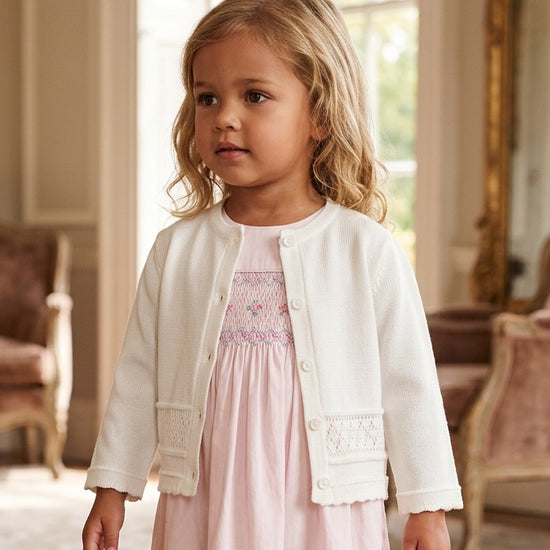 Carriage Boutique white knit cardigan worn by a young girl over a pink dress in a classic indoor setting