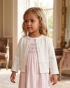 Carriage Boutique white knit cardigan worn by a young girl over a pink dress in a classic indoor setting