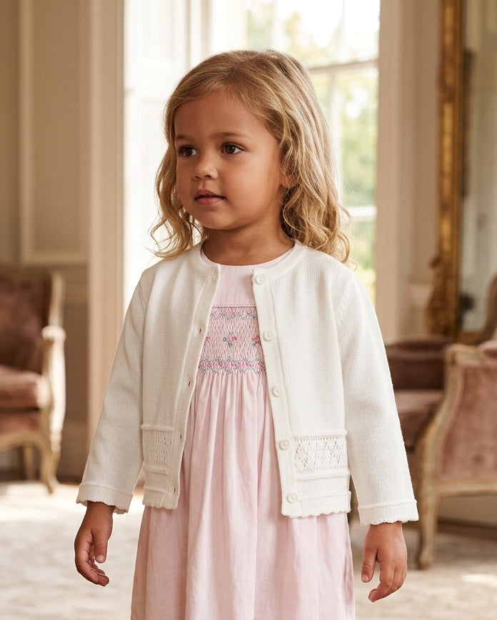 Carriage Boutique white knit cardigan worn by a young girl over a pink dress in a classic indoor setting
