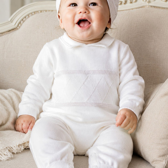 Carriage Boutique white knit diamond stitch baby boy christening outfit with matching hat on a seated baby
