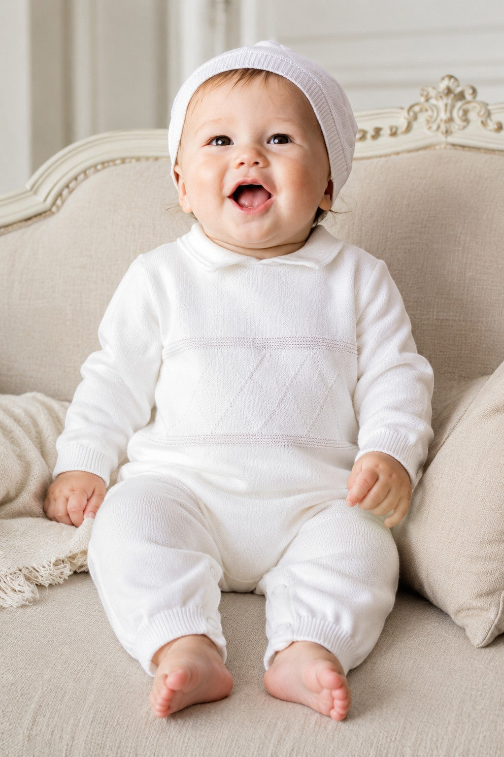 Carriage Boutique white knit diamond stitch baby boy christening outfit with matching hat on a seated baby