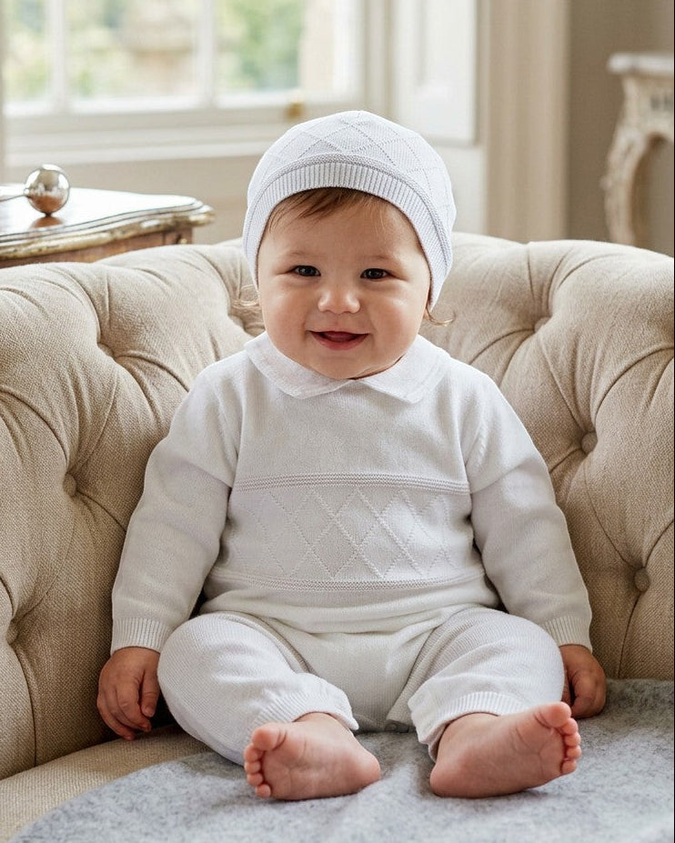 Carriage Boutique white knit diamond stitch baby boy christening outfit with matching hat on a tufted chair
