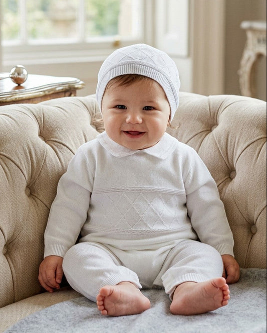 Carriage Boutique white knit diamond stitch baby boy christening outfit with matching hat on a tufted chair