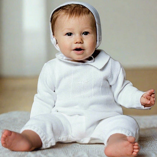Baby boy wearing a white Carriage Boutique knit cotton christening outfit with a matching bonnet and knitted collar.