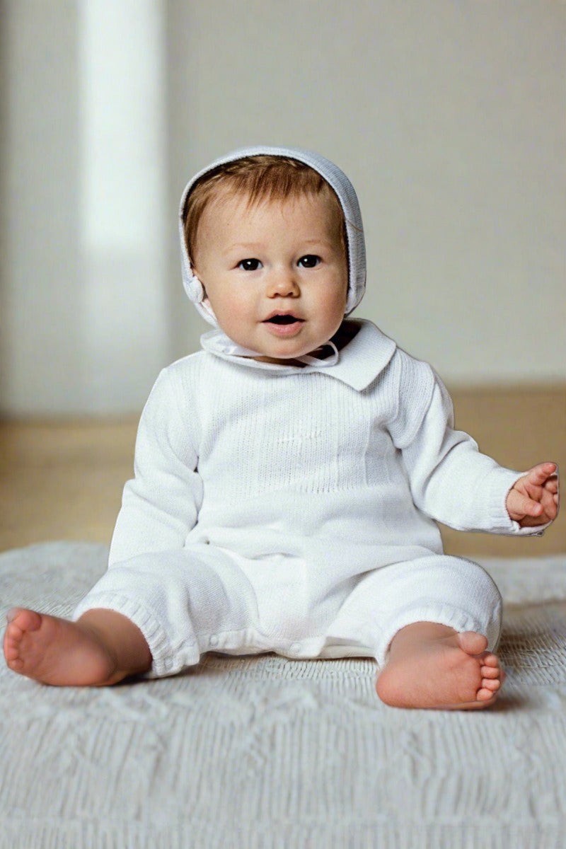Baby boy wearing a white Carriage Boutique knit cotton christening outfit with a matching bonnet and knitted collar.