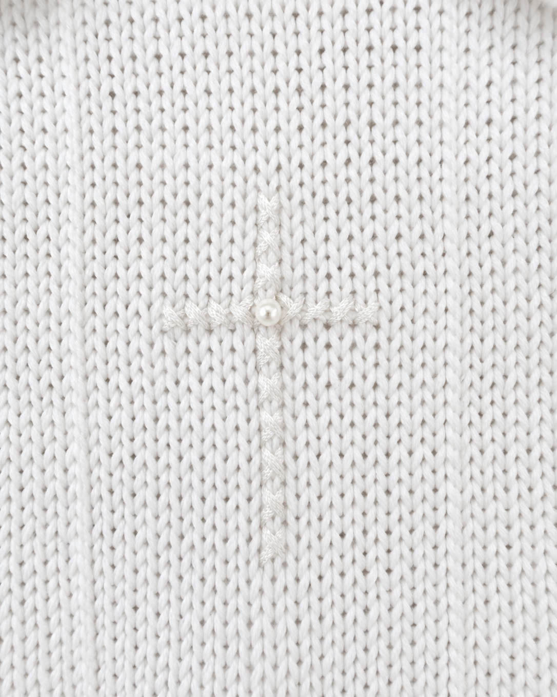 Close-up of Carriage Boutique white knit cotton christening outfit featuring an embroidered cross with a center pearl.
