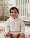 Carriage Boutique white knit hooded baby sweater made of soft cotton worn by a smiling baby in a nursery.