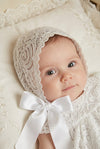 Carriage Boutique baby girl wearing an elegant white lace baptism bonnet with a soft satin ribbon tie.