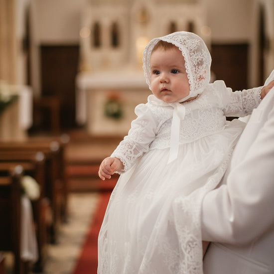 Carriage Boutique baby girl wearing a white long sleeve lace christening gown and matching bonnet in a church